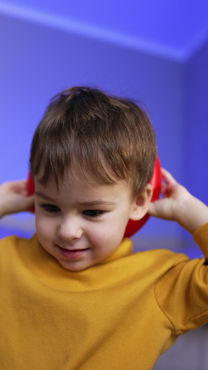 Bambino carino con capelli castani che indossa un maglione giallo. Un ragazzino tiene un anello rosso di una piramide dietro la testa. Angolazione dal basso. Video verticale