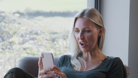 woman in chair by window at home having video call on mobile phone