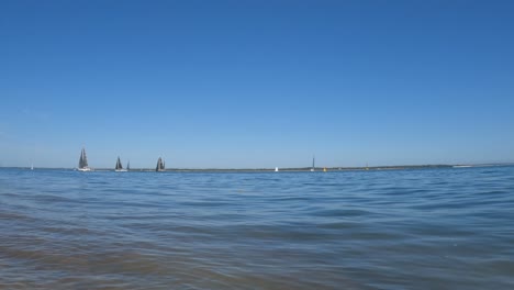 Sailing-boats-gently-sailing-in-the-calm-blue-sea-with-the-blue-sky-in-the-background