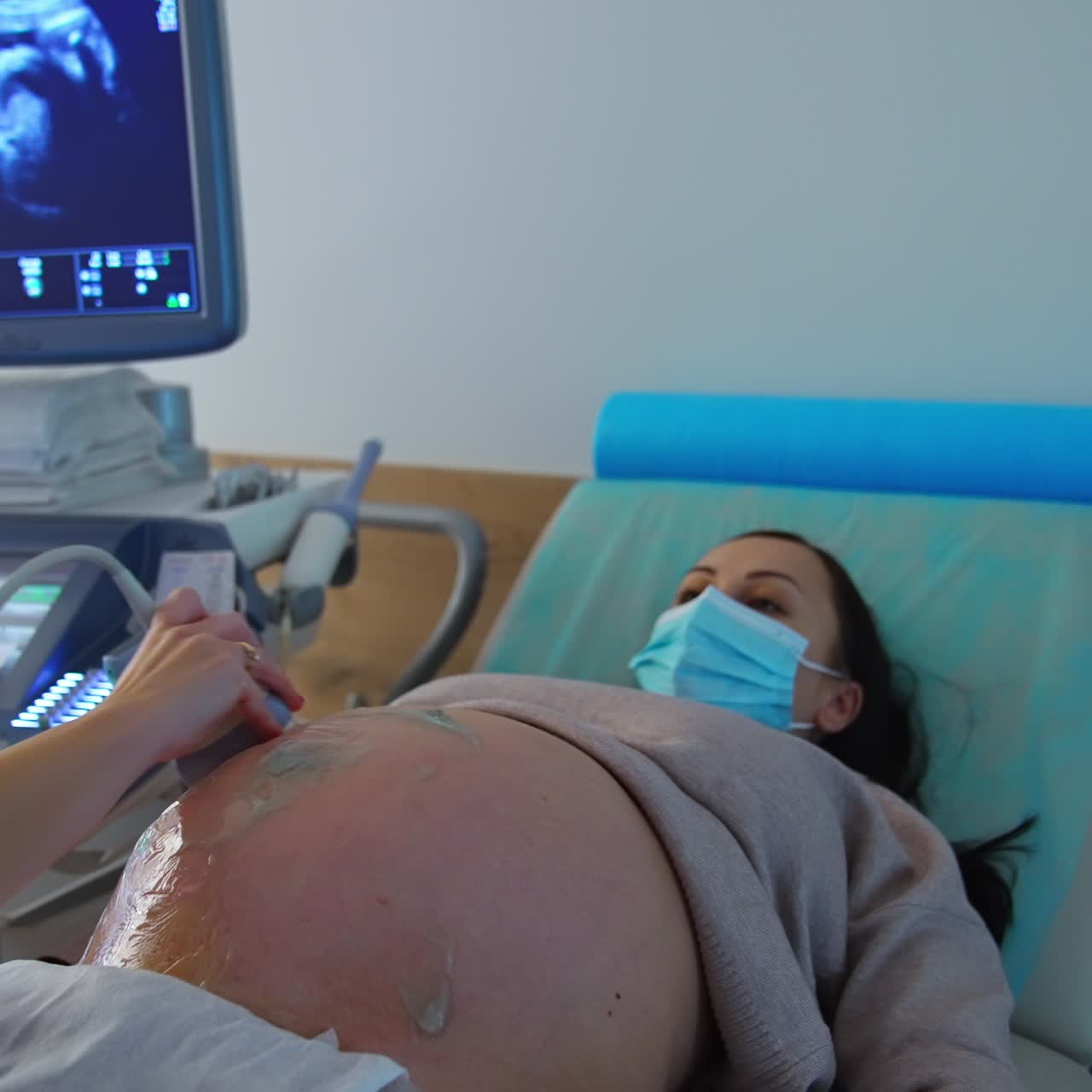 Donna con il pancione negli ultimi mesi di gravidanza si sottopone a un'ecografia. La mano del medico muove il dispositivo sull'addome coperto di gel