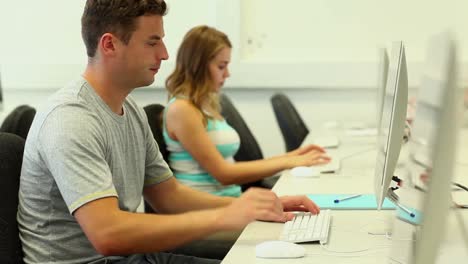 Dos-Estudiantes-Enfocados-Trabajando-En-La-Sala-De-Computadoras