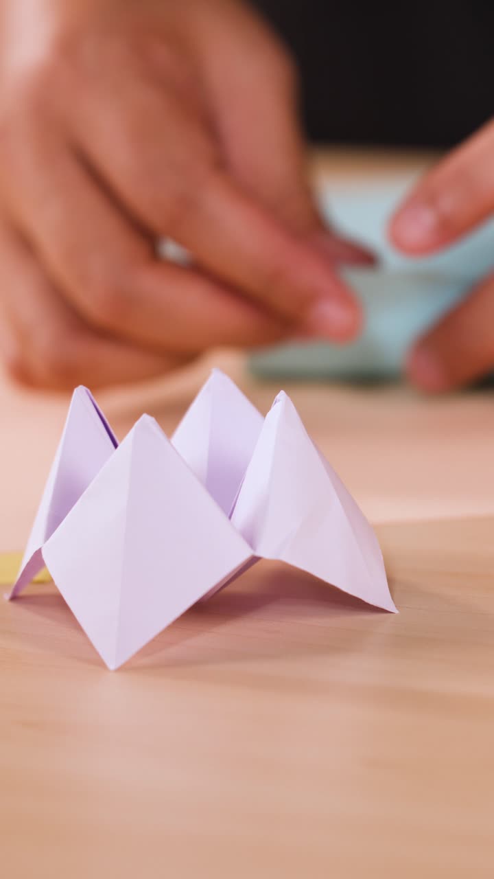 Una persona piega con attenzione della carta blu dietro un origami della fortuna bianco su legno