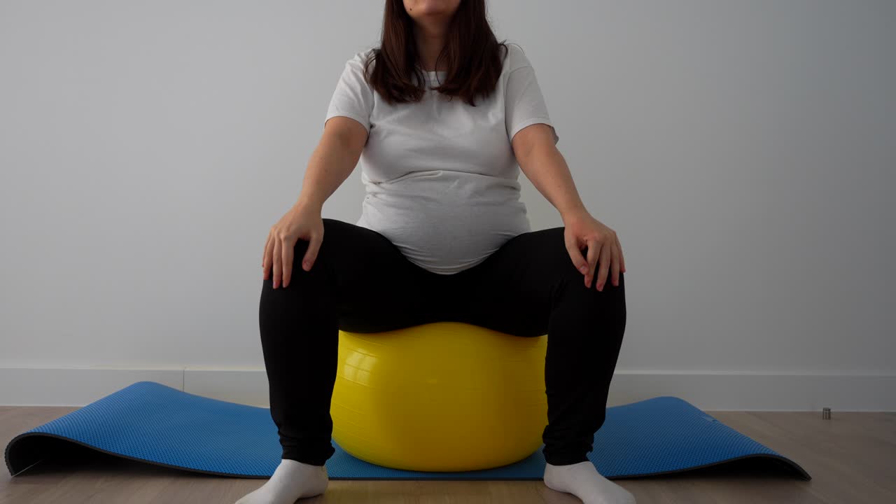 Pregnant woman standing on a fitball to do useful exercises for the baby delivery