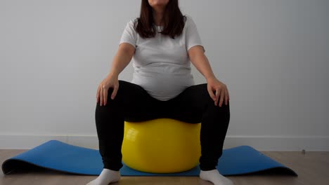 pregnant woman standing on a fitball to do useful exercises for the baby delivery