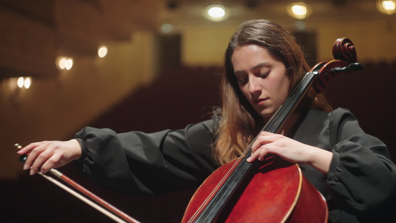 una mujer solitaria está tocando el violonchelo en un salón de música, ensayando o en un concierto de música clásica.