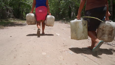 women in honduras cary heavy water jugs on a dirt road