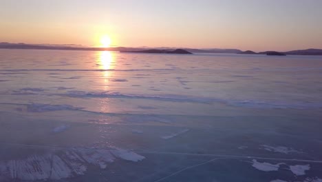 drone volando bajo sobre agua helada en rusia, famoso lago baikal en invierno con gran puesta de sol