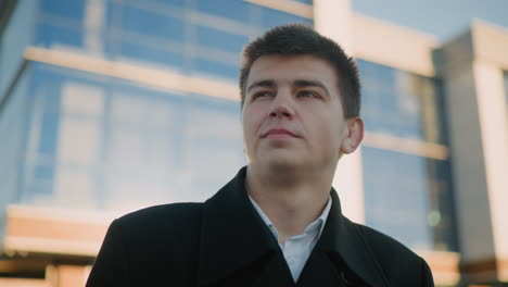 man in black clothing checks wristwatch with subtle smile while sunlight reflects off his shoulder, exuding confidence and precision, background features modern glass building