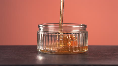 SUPER-SLOW-MOTION-CU-Honey-is-being-poured-into-glass-jar-against-bright-background