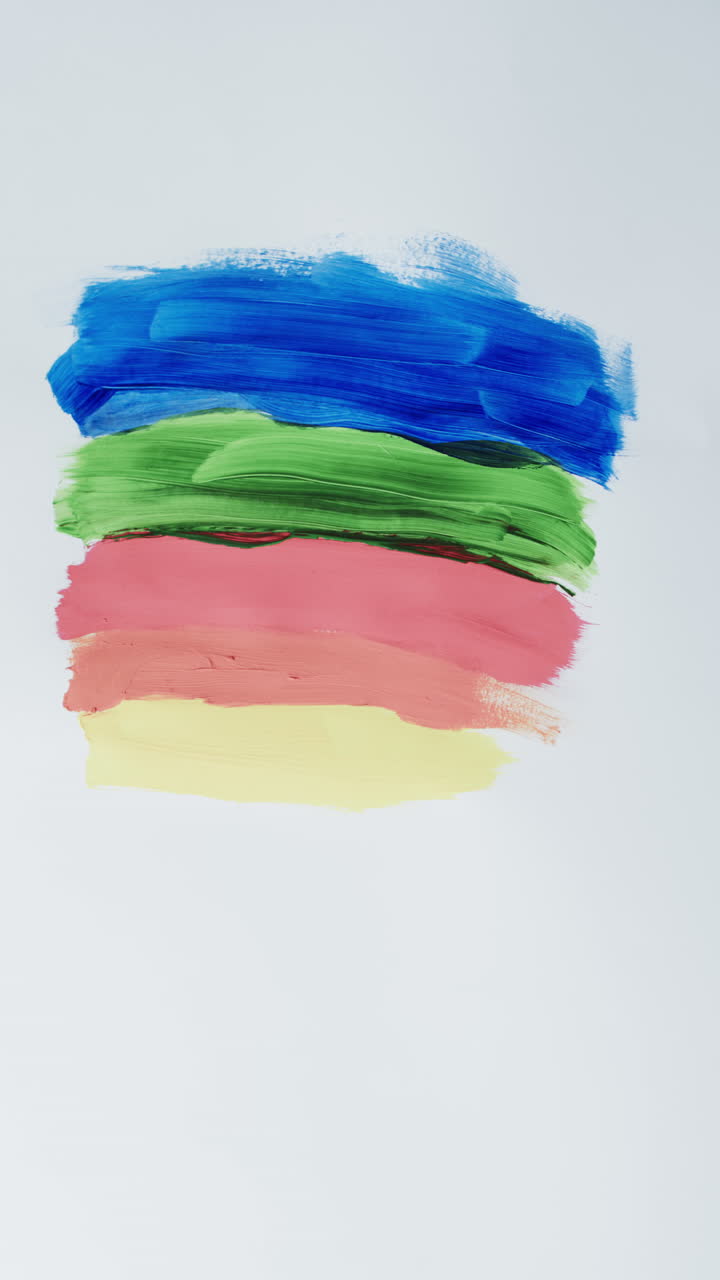 Vertical video of multi coloured paint stripes on white background with copy space, slow motion