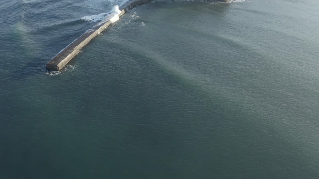 Ocean waves rolling over breakwater structure near Saint-Jean-de-Luz harbor entrance, blue water, France. Aerial drone top-down view, copy space