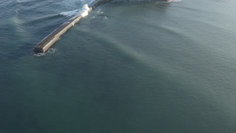 ocean waves rolling over breakwater structure near saint-jean-de-luz harbor entrance, blue water, france. aerial drone top-down view, copy space
