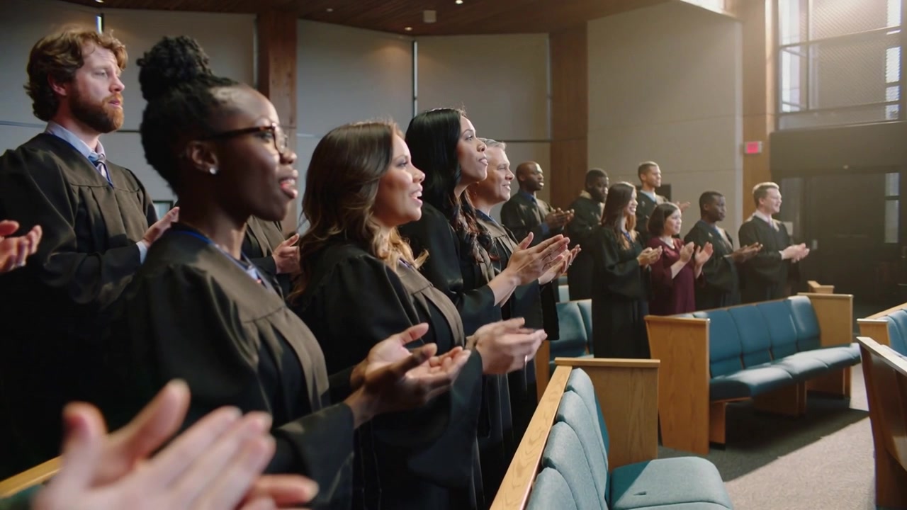 Membri del coro che applaudono e cantano in chiesa mentre il servizio inizia, con abiti neri e alte finestre.