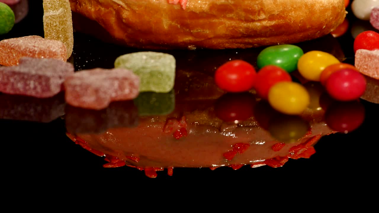 rosado gracioso sorprendido rosquilla esmaltada con salpicaduras, dulces de caramelo a rayas, dragee colorido con pasas o cacahuetes en el interior sobre fondo negro