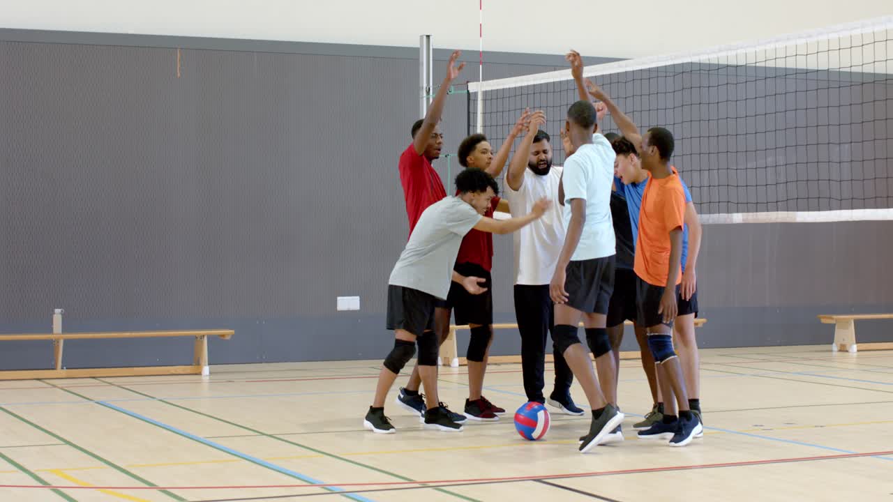 Male teammates huddling on volleyball court with leader speaking, cheering and readying play
