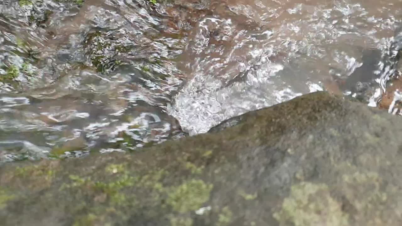 이끼가 있는 거대한 사암 석판 아래로 흐르는 산 샘물에서 나오는 작은 폭포의 느린 동작 영상, 맑은 식수, 고요하고 평화로운 명상