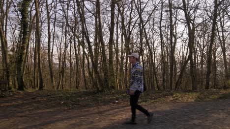 young caucasian man in a long arm shirt walking through a bare deciduous forest at sunset