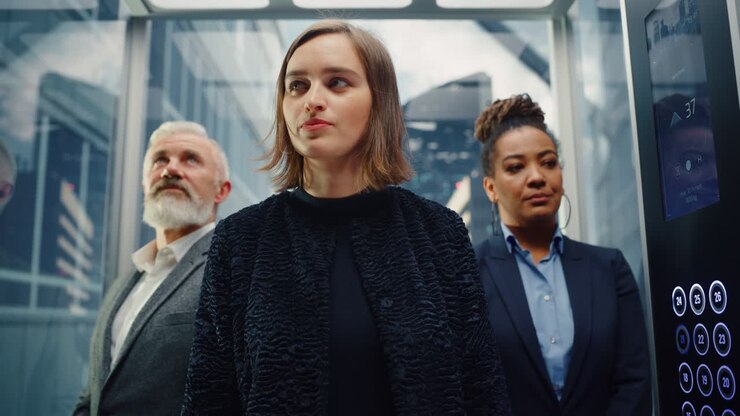 Three Diverse Multiethnic International People Ride a Glass Elevator to Office in a Modern Business Center. Focus on a Happy Young Beautiful Businesswoman Standing in Front in a Lift.