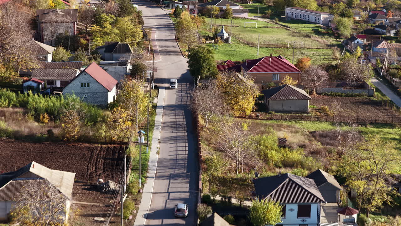 Aerial drone view of a quiet Moldovan village street with traditional houses, gardens, and trees during autumn