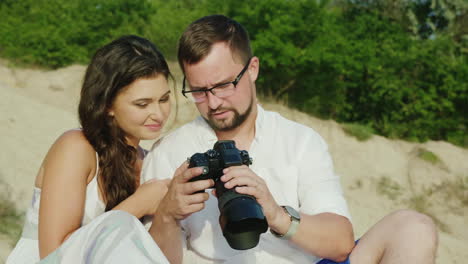 a young couple looks at the pictures on a digital camera sit next to the beach great memories from h