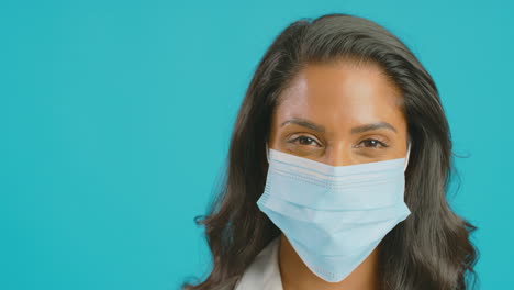 Primer-Plano-Retrato-De-Una-Enfermera-Uniformada-Con-Mascarilla-Delante-Del-Fondo-Azul-Del-Estudio