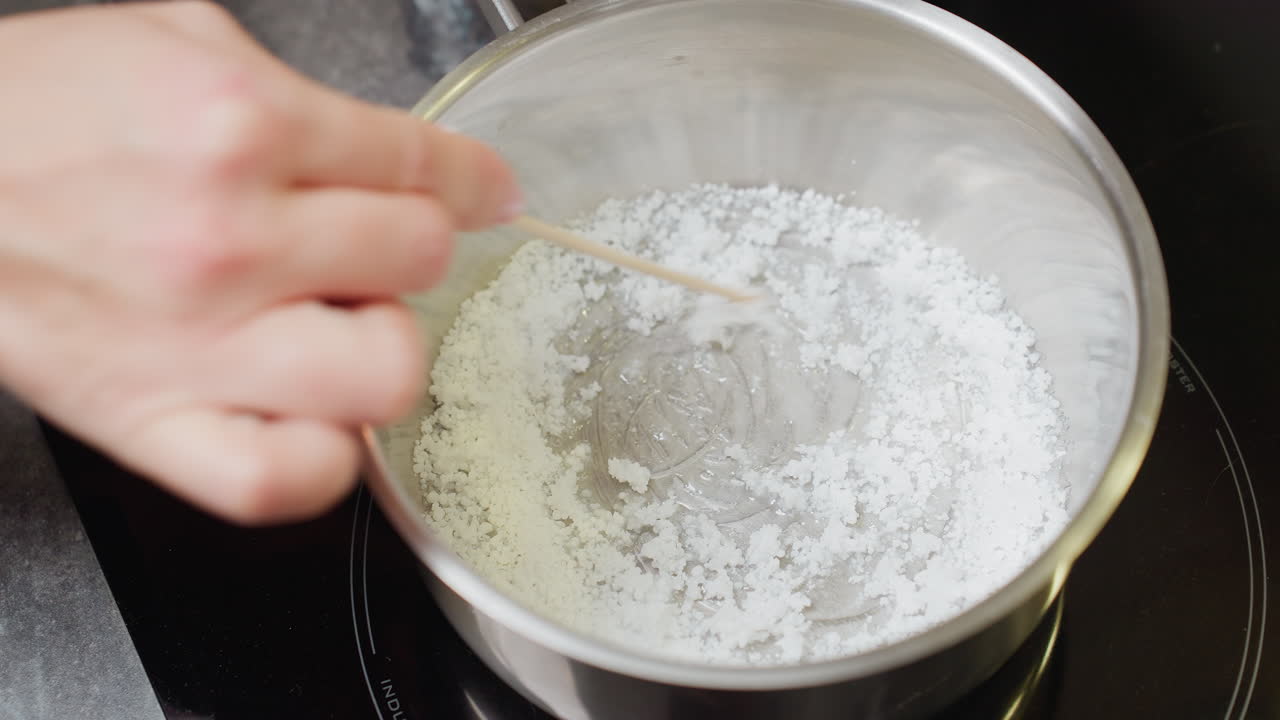 vista a mano de la dama moviendo el azúcar en la olla, proceso de cocción en la estufa, centrarse en el manejo de ingredientes, preparación para hornear o creación de platos dulces en un entorno de cocina bien iluminado