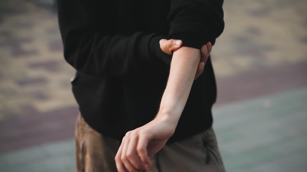 若い白人男性がタイル張りの舗装で両手をすぼめて何かを差し出したり、袖をまくりながら手品を練習したりしている。微妙な手首の動きと集中した指先、コイン手品を練習するストリートパフォーマー、ボランティア