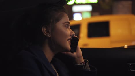 chica sonriente feliz viajando en un taxi por la noche sentada en el asiento trasero y hablando en el teléfono inteligente. mujer feliz en el taxi. noche