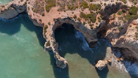 Drone-De-Arriba-Hacia-Abajo,-Costa-Escénica-De-Praia-Da-Marinha-Al-Mediodía,-Sombras-En-El-Océano