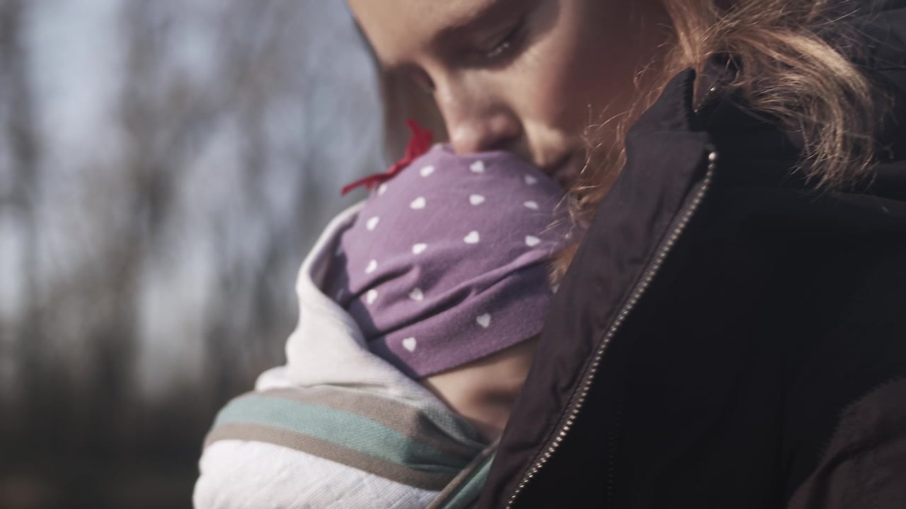 Madre tiene in braccio un bambino che dorme nel marsupio e lo coccola in una giornata fredda, primo piano