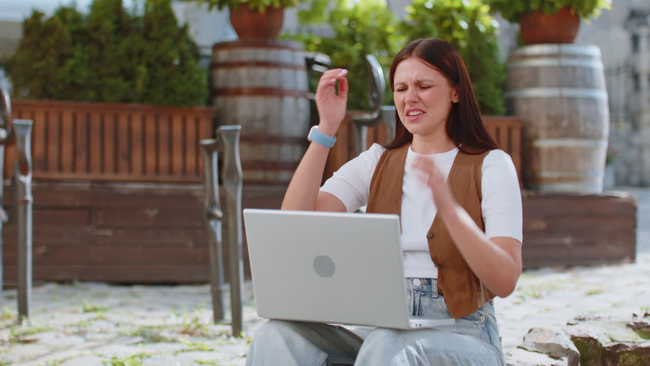 Caucasian young woman using laptop browsing loses lottery results bad news sitting in city street