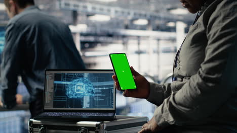 technician using green screen smartphone in server hub while optimizing ai