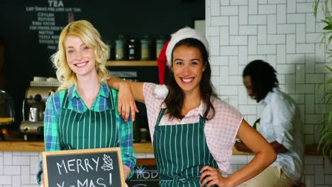 portrait of waitress and coworker standing with merry x mas board