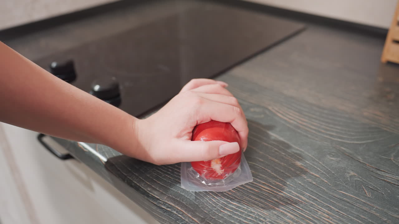 close up hand view of woman with fixed nail tapping wooden kitchen countertop as another person pushes hotdog package toward her and she collects it showing food handling gesture