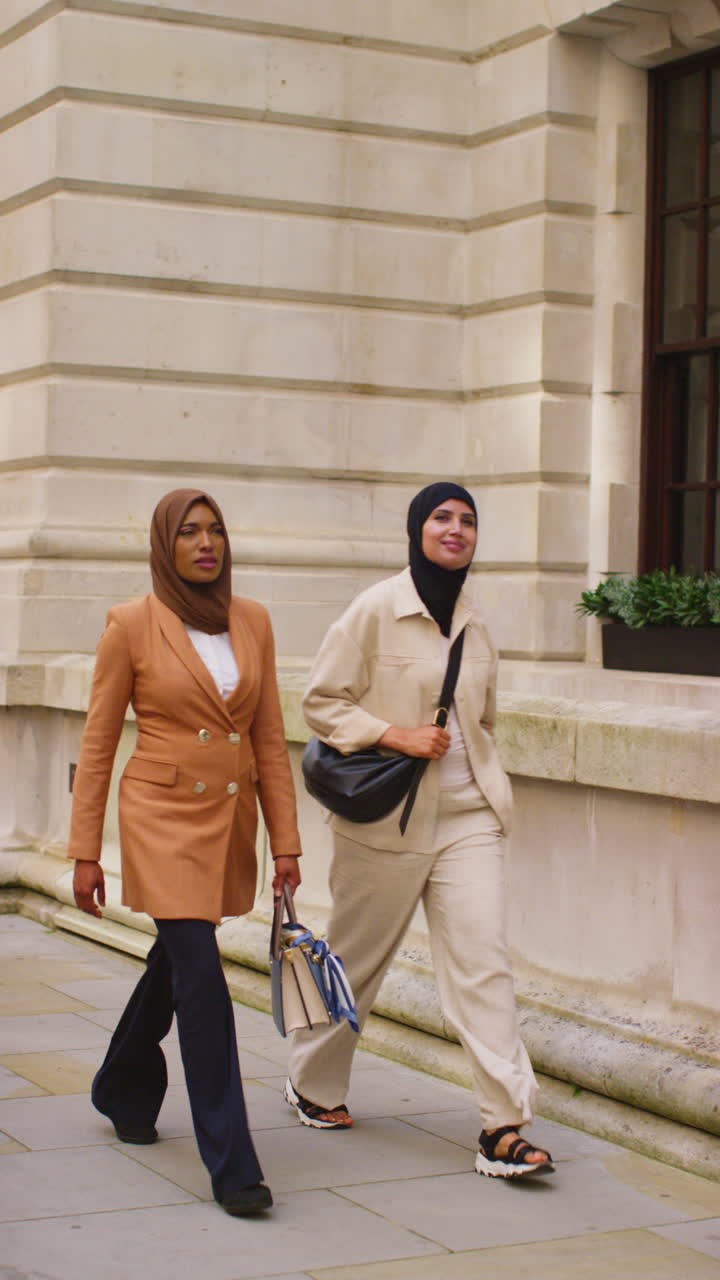 Vertical Video Of Two Muslim Businesswomen Wearing Hijabs With Modern Business Suits Walking To Work Past City Office Buildings 2