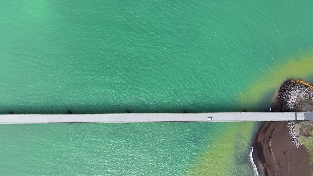 Drone video looking straight down at a vehicle crossing a bridge over the flowing turquoise waters of the Olfusa River in southern Iceland