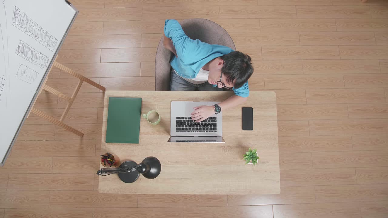 집에서 스마트폰 에 노트북으로 타이핑하는 화이트보드 에 나무 책상에 앉아있는 아시아 남자의 허리 통증의 상단 뷰
