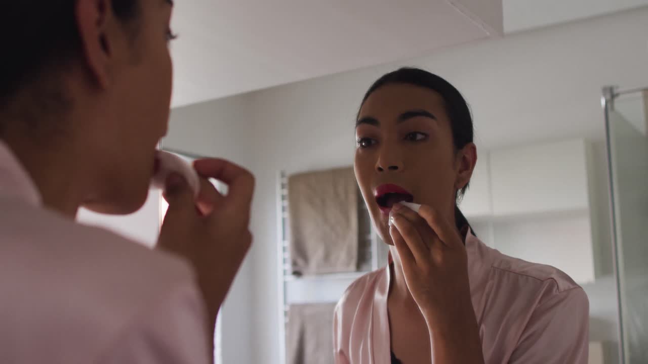 Mixed race gender fluid person standing in bathroom and using a lipstick
