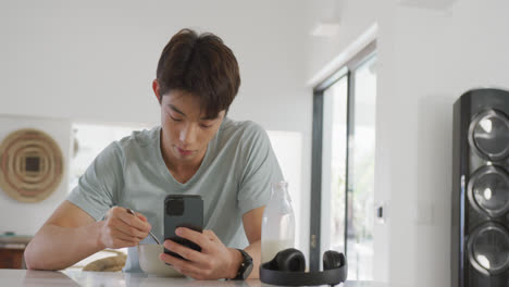 asian boy using smartphone while having breakfast in living room at home