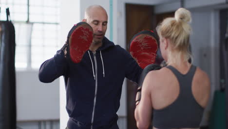 caucasian female boxer wearing boxing gloves training her punches with male trainer at the gym