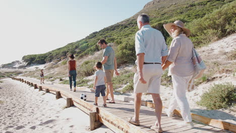 multi-generation family on summer vacation walking along wooden boardwalk on way to beach