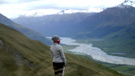 niña mirando un hermoso valle verde con montañas con un río que atraviesa en un día soleado brillante en una colina cubierta de hierba en un día ventoso, a la deriva gran tiro de mano