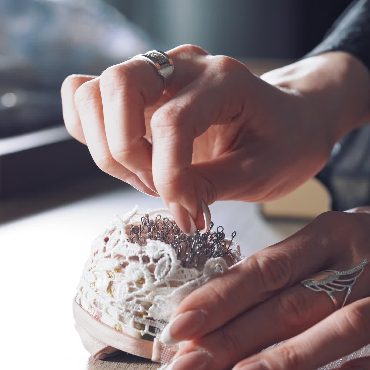 Young tailor is taking spoos from the beautiful pincushion. Many black sewing pins in a small white pillow for seamstress on the wooden table.