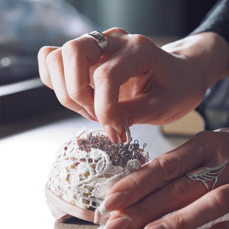 young tailor is taking spoos from the beautiful pincushion. many black sewing pins in a small white pillow for seamstress on the wooden table.