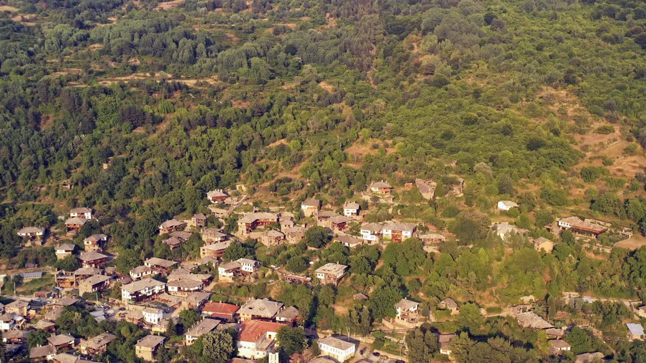 revelación aérea lenta de colinas cubiertas de árboles sobre casas de aldeas de montaña de kovachevitsa rhodopes bulgaria