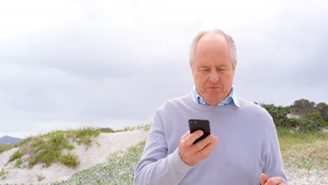 Vista-Frontal-De-Un-Anciano-Caucásico-Usando-Un-Teléfono-Móvil-En-La-Playa-4k