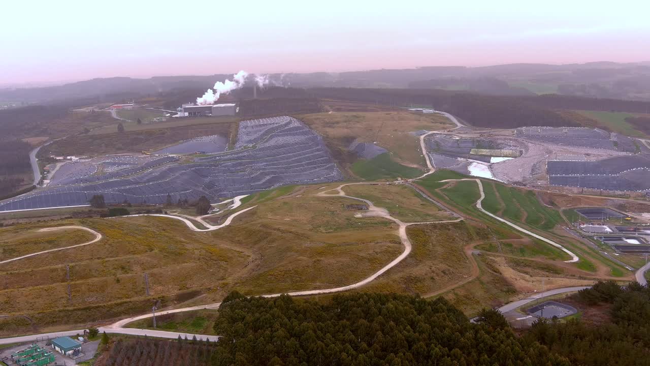 dolly aéreo sobre vertedero de reciclaje de residuos con humo saliendo del edificio en la distancia