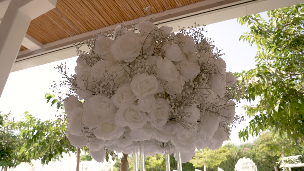 Una splendida composizione di rose bianche e verde delicato è elegantemente disposta sopra uno spazio esterno, creando un'atmosfera serena e romantica per qualsiasi evento.