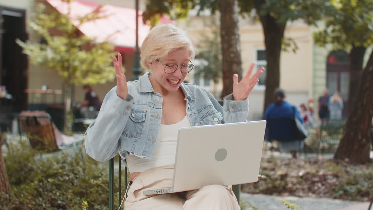 una joven feliz que trabaja en una computadora portátil gritando de alegría levanta las manos en la calle de la ciudad