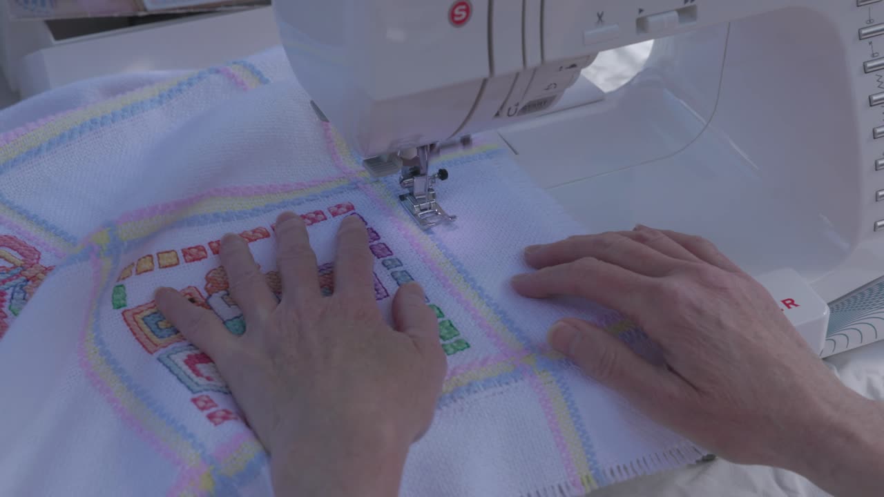 establishing shot of a seamstress working on a baby blanket with symbols